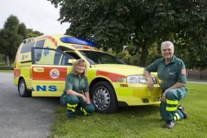 Två ambulanspersonal sitter framför en ambulans. Foto.