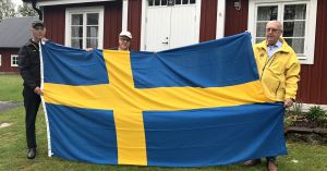 Representanter från Glimåkra hembygdsförening håller i en svensk flagga tillsammans med Uno Johansson från Lions Club Östra Göinge.