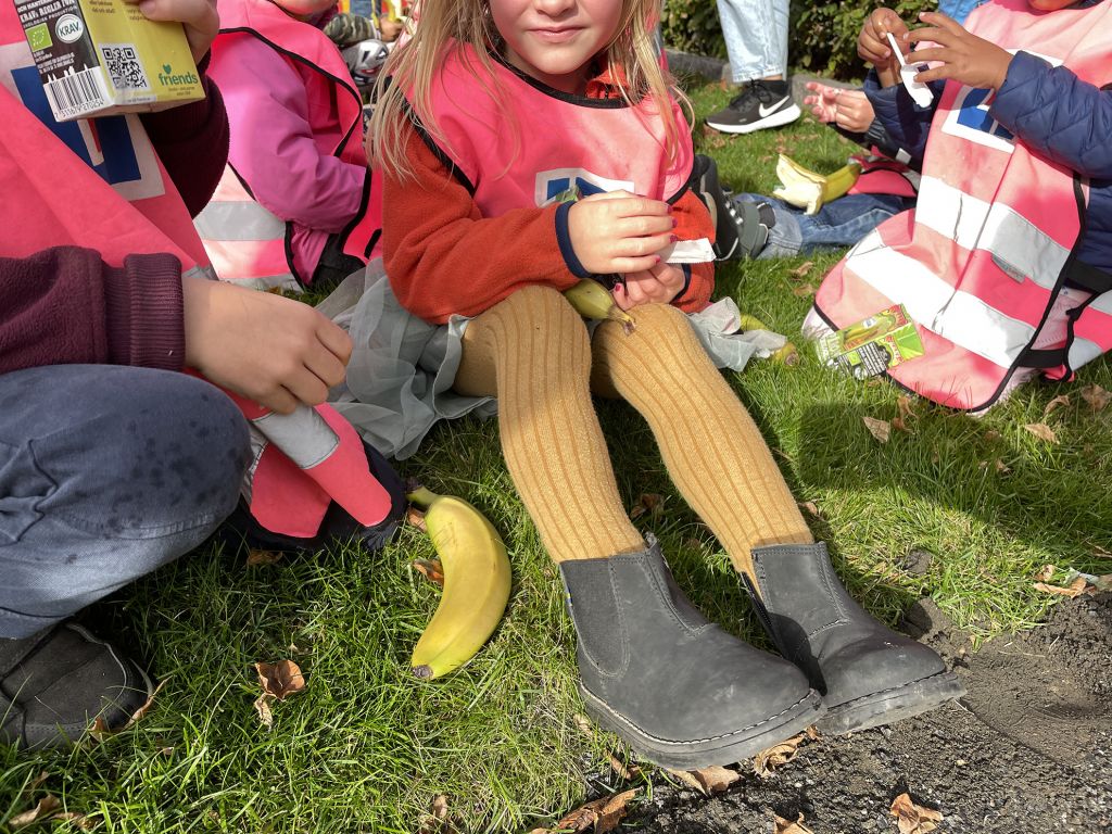 Närbild på barn som sitter p gräsmattan och fikar med festis och banan.