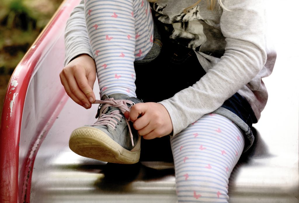 Bild på barn som sitter på rutschbana och knyter sina skor. 