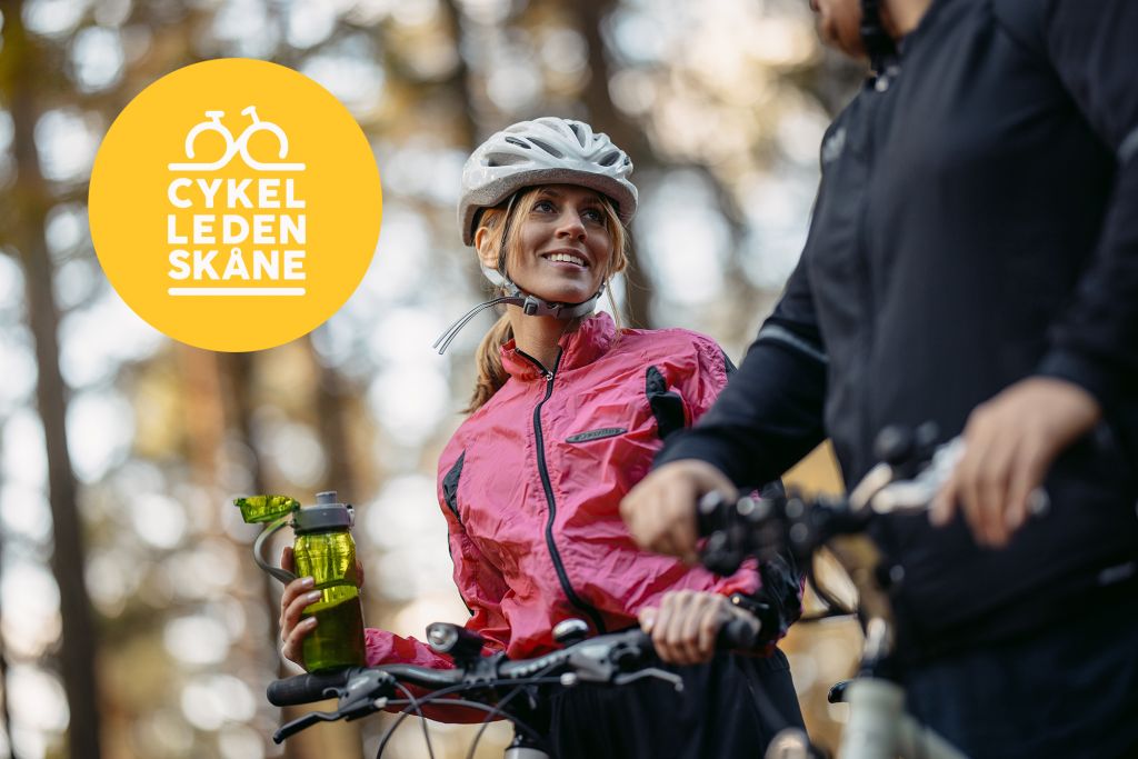 Bild på tjej med cykel som tittar på annan person med cykel. Tillsammans med gul cirkel och loggan för Cykelleden Skåne.