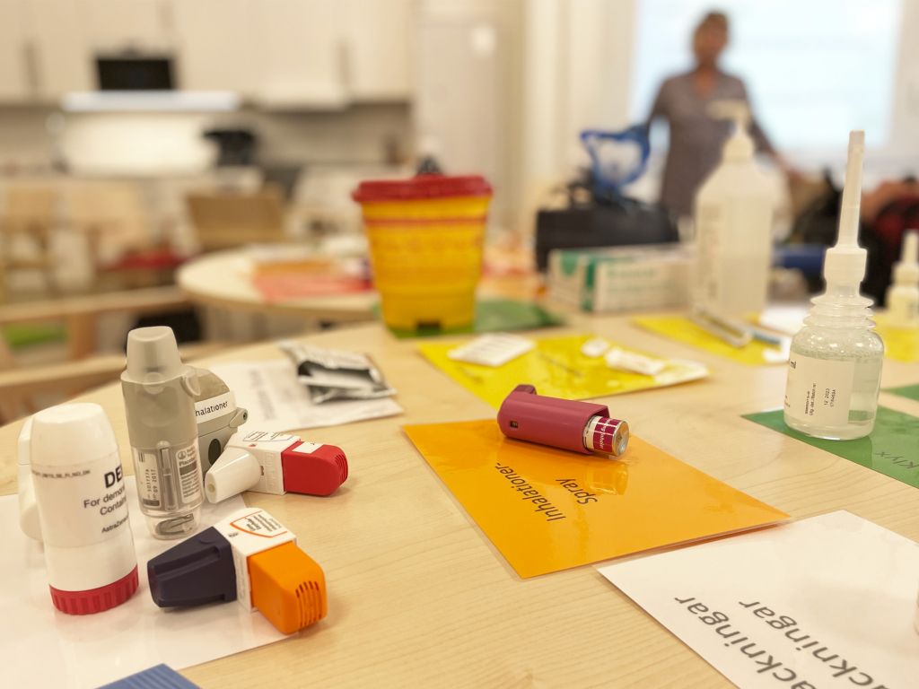 Bild på läkemedel på ett bord tillsammans med etiketter. Pernilla skymtas i bakgrunden.