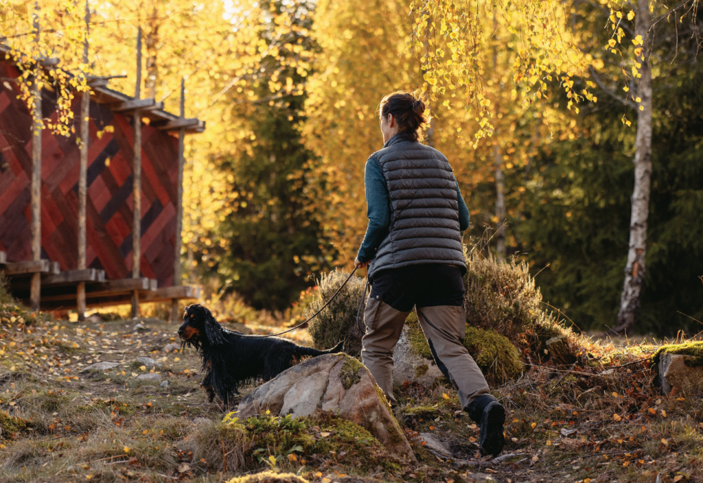 Bild på kvinna som vandrar i en skog med sin hund.