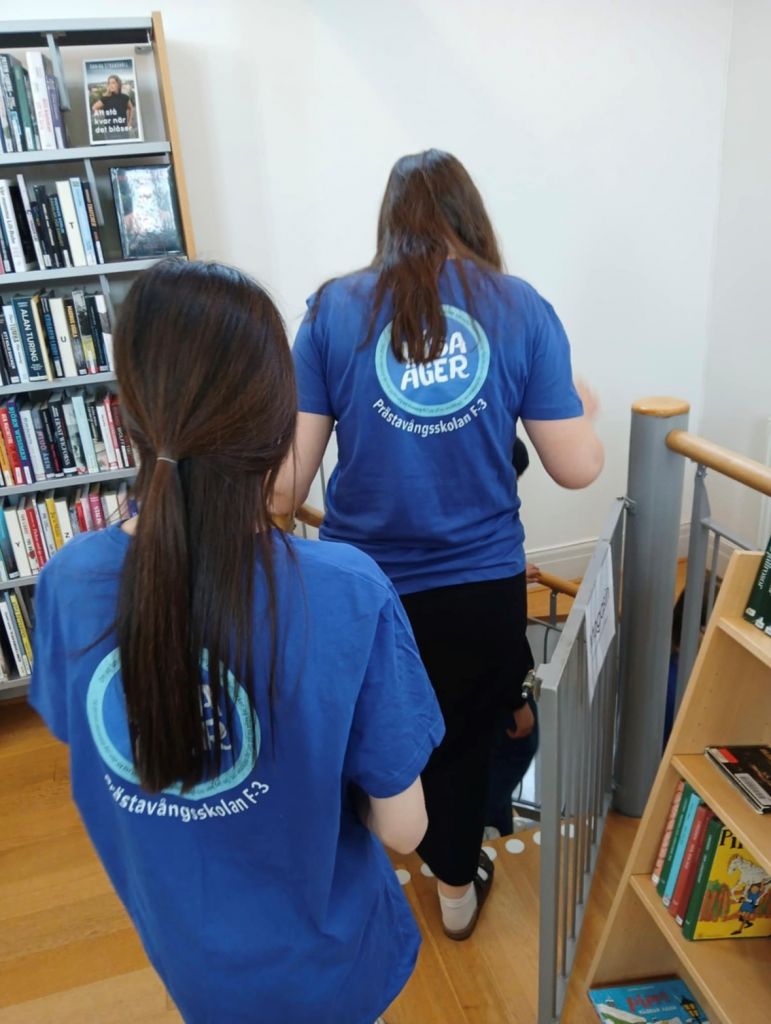 Bild på två unga tjejer med blå-t-shirts i ett bibliotek.