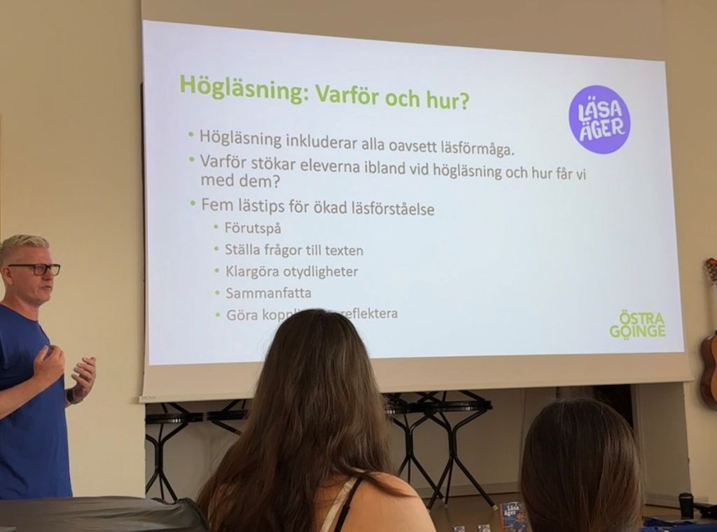 Bild på person som står framför en stor powerpointpresentation.